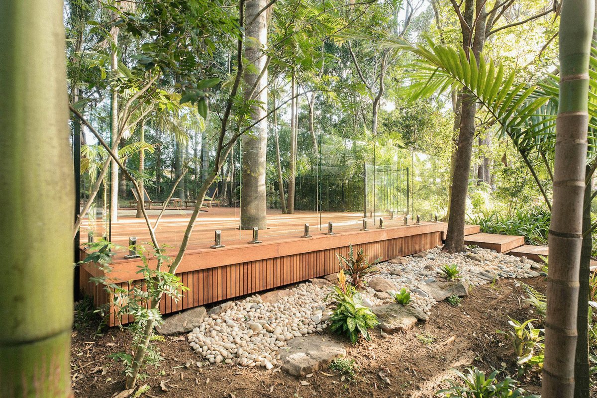A timber deck with glass panels along its edge, surrounded by trees, rocks and plants.