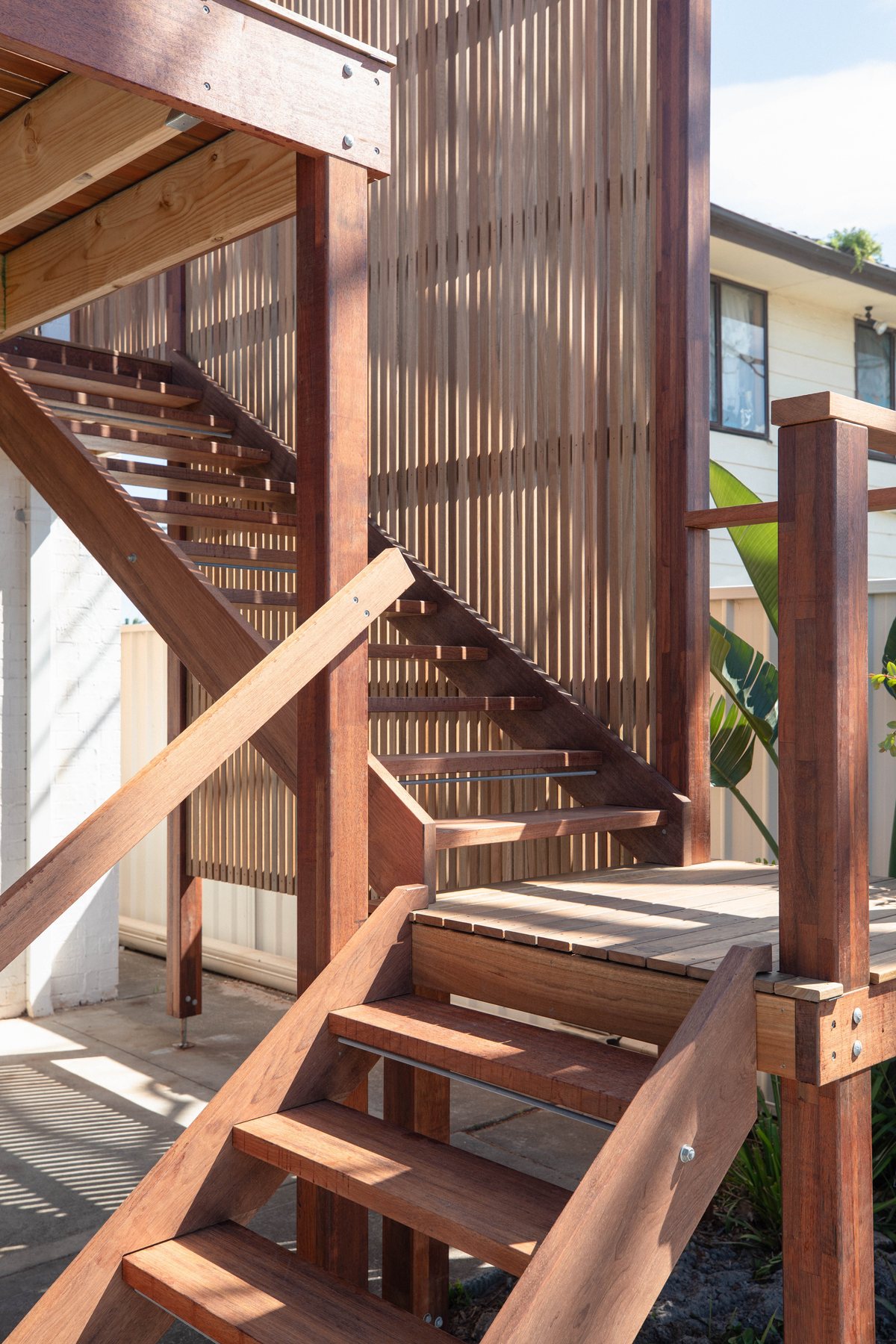 Timber stairs turn through a landing beside a tall vertical slatted screen.