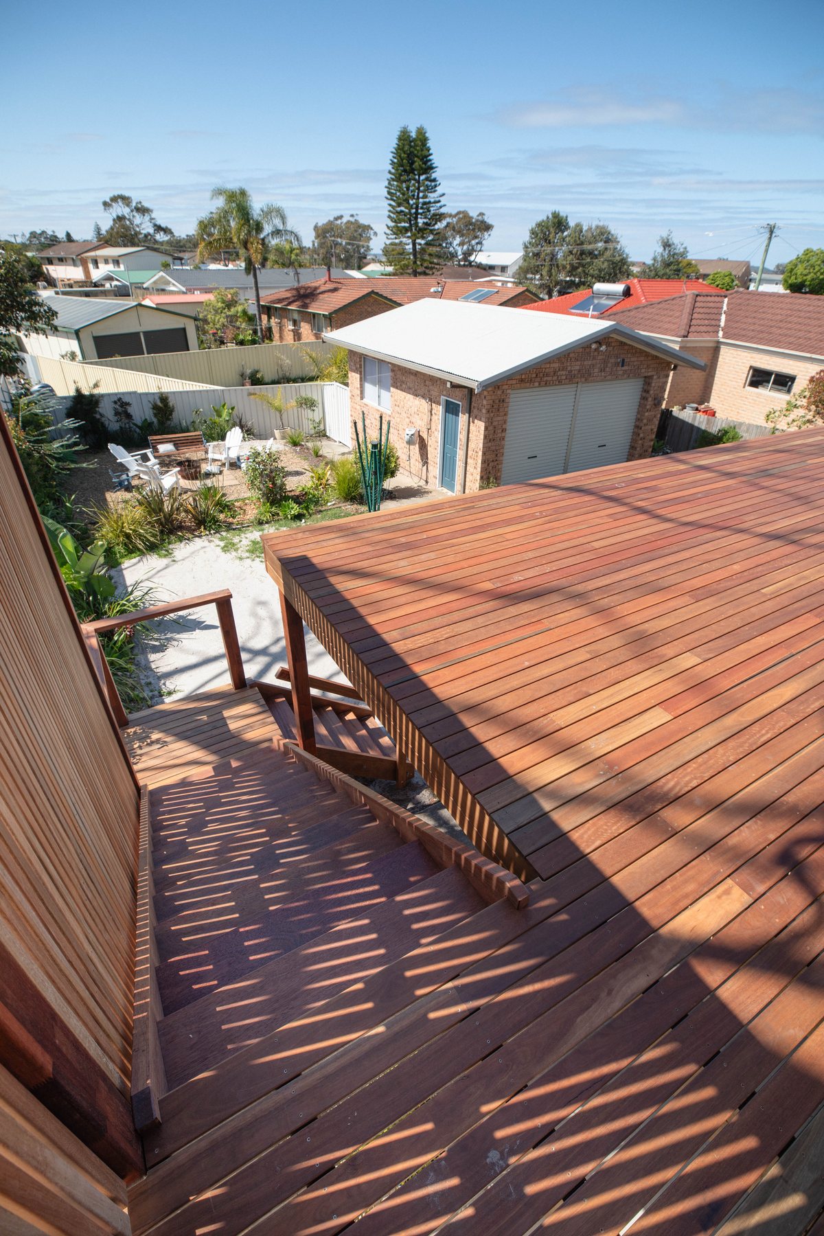 A timber deck beside a house, with stairs descending along the wall towards the garden.