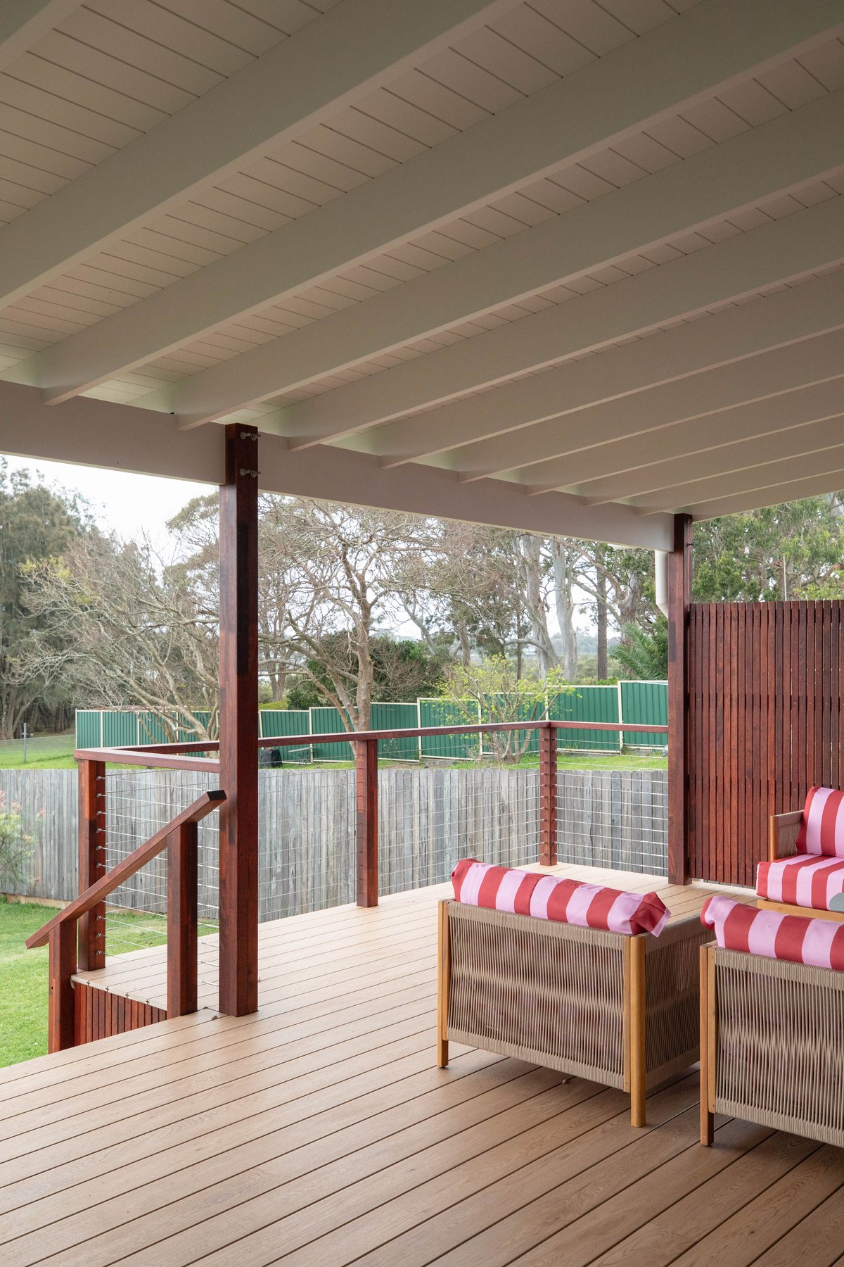 A covered timber deck with a white ceiling, timber posts and outdoor chairs beside a slatted screen.