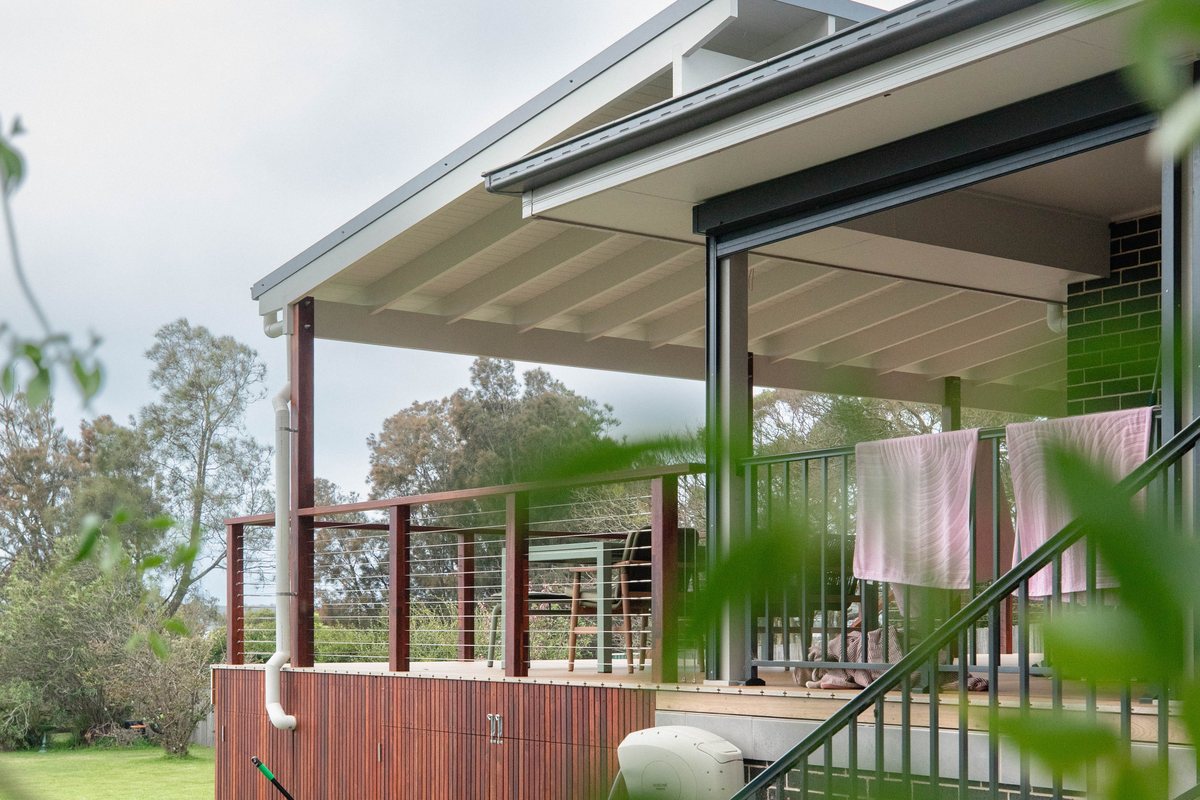 A covered deck with a white gable roof, timber posts and wire balustrades beside the house.