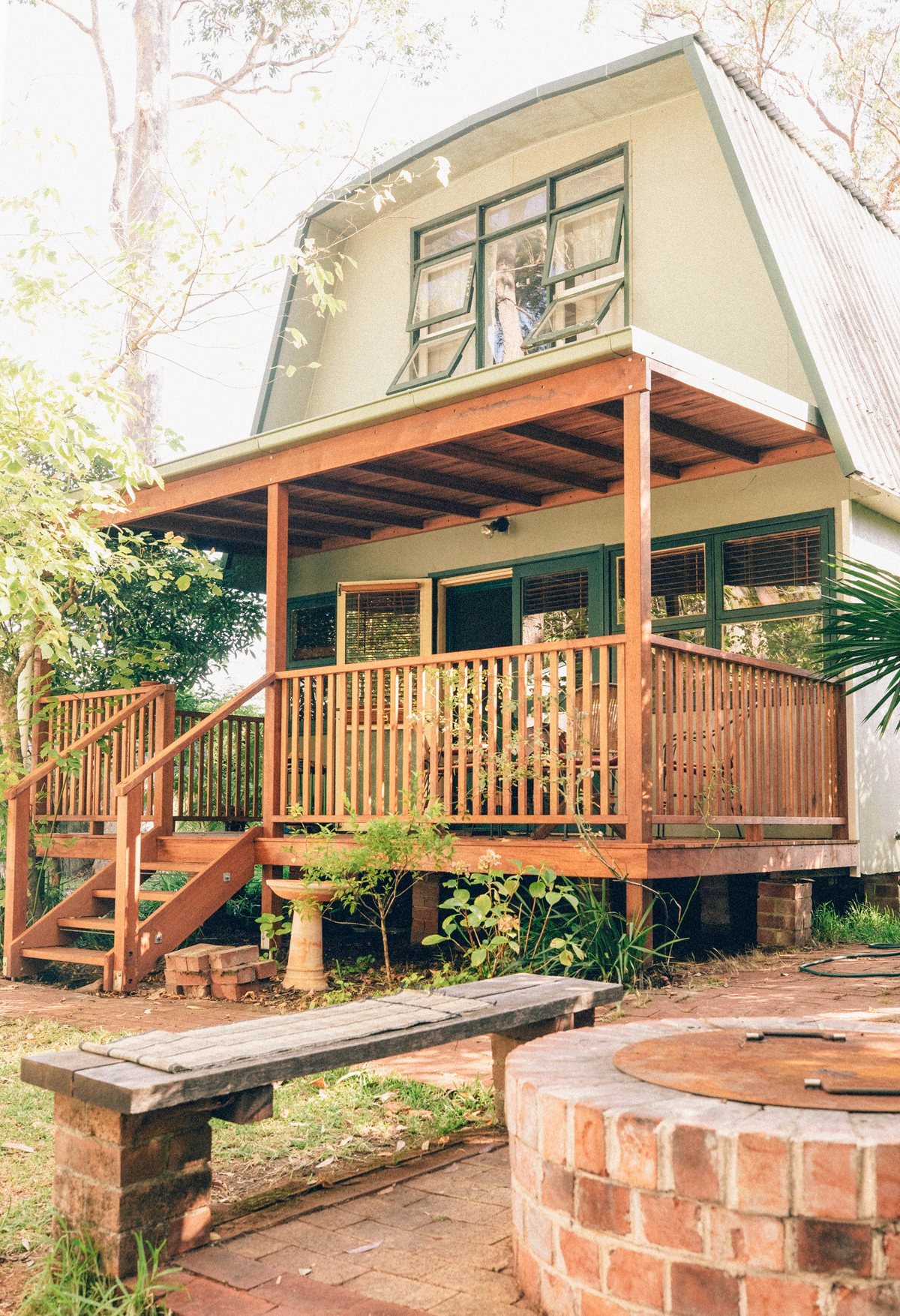 A timber verandah with a shallow roof, vertical balustrade boards and steps beside a house.