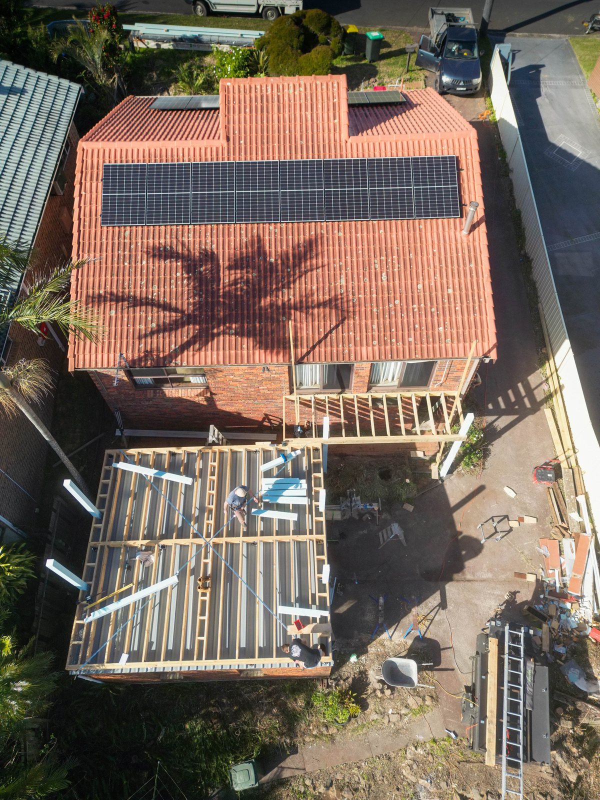 An aerial view of exposed framing beside a brick house, with construction materials around it.