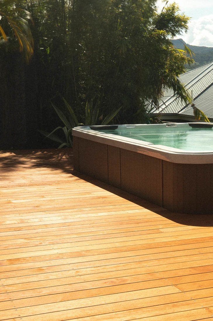 Timber decking beside a raised spa, with trees around the edge of the space.