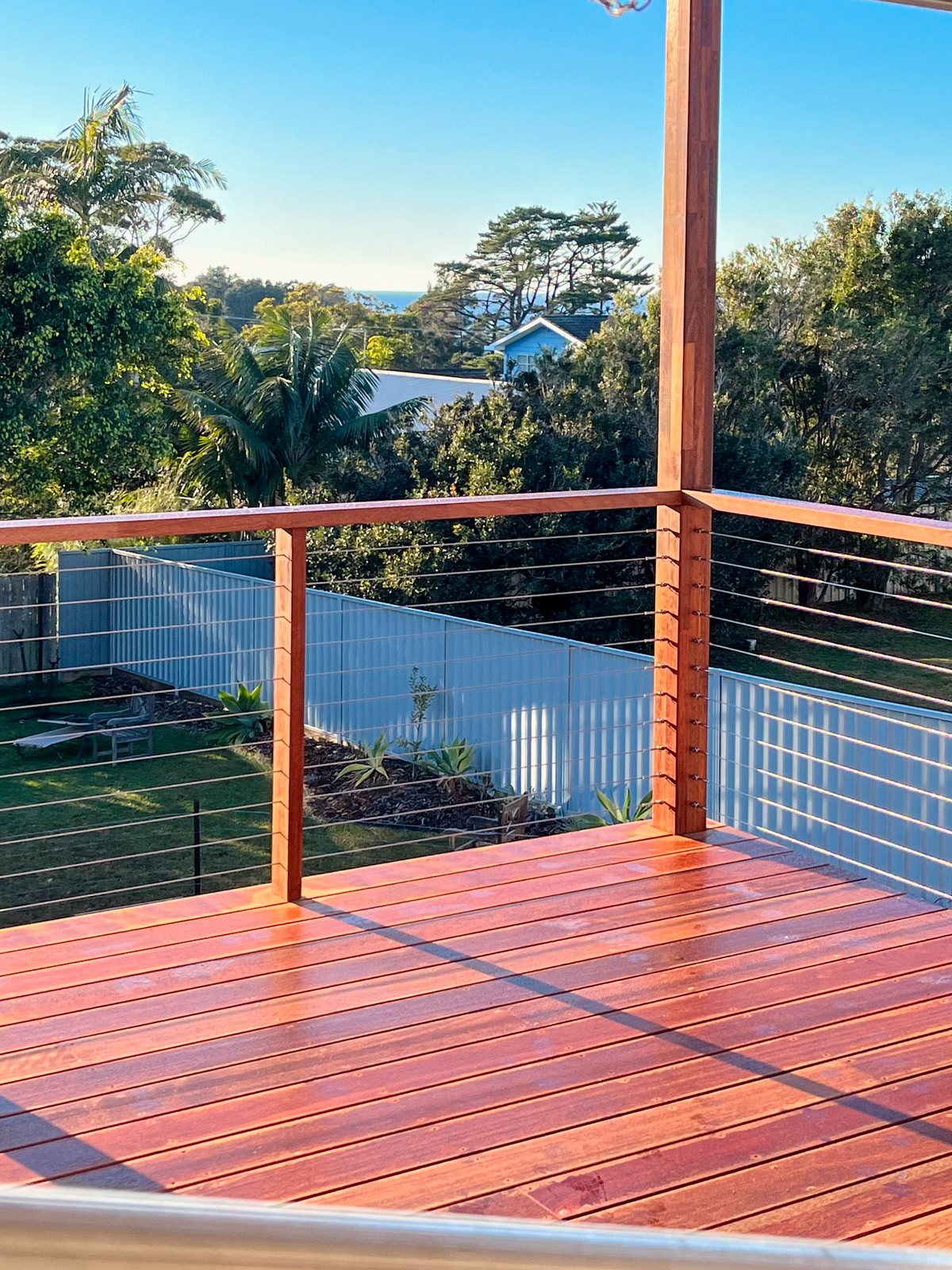 A sunlit timber deck corner with horizontal wires between timber balustrade posts.