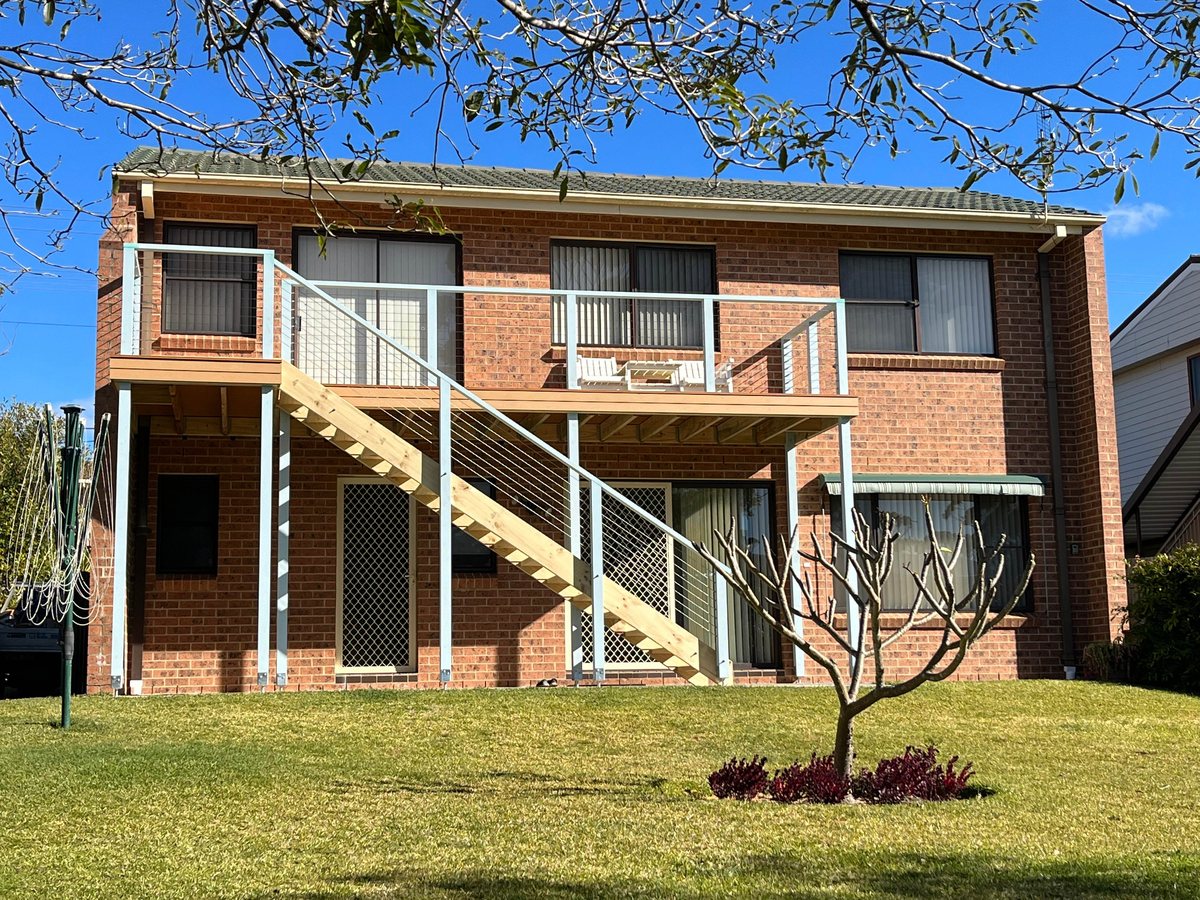 An elevated deck and straight timber stairs with pale posts and wire rails beside a brick house.