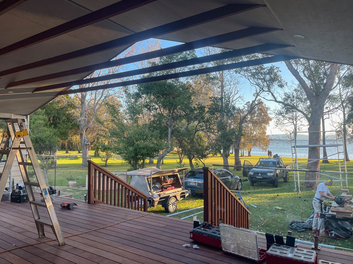 A timber deck beneath a pitched roof, with a ladder, open tool cases and a stair opening.