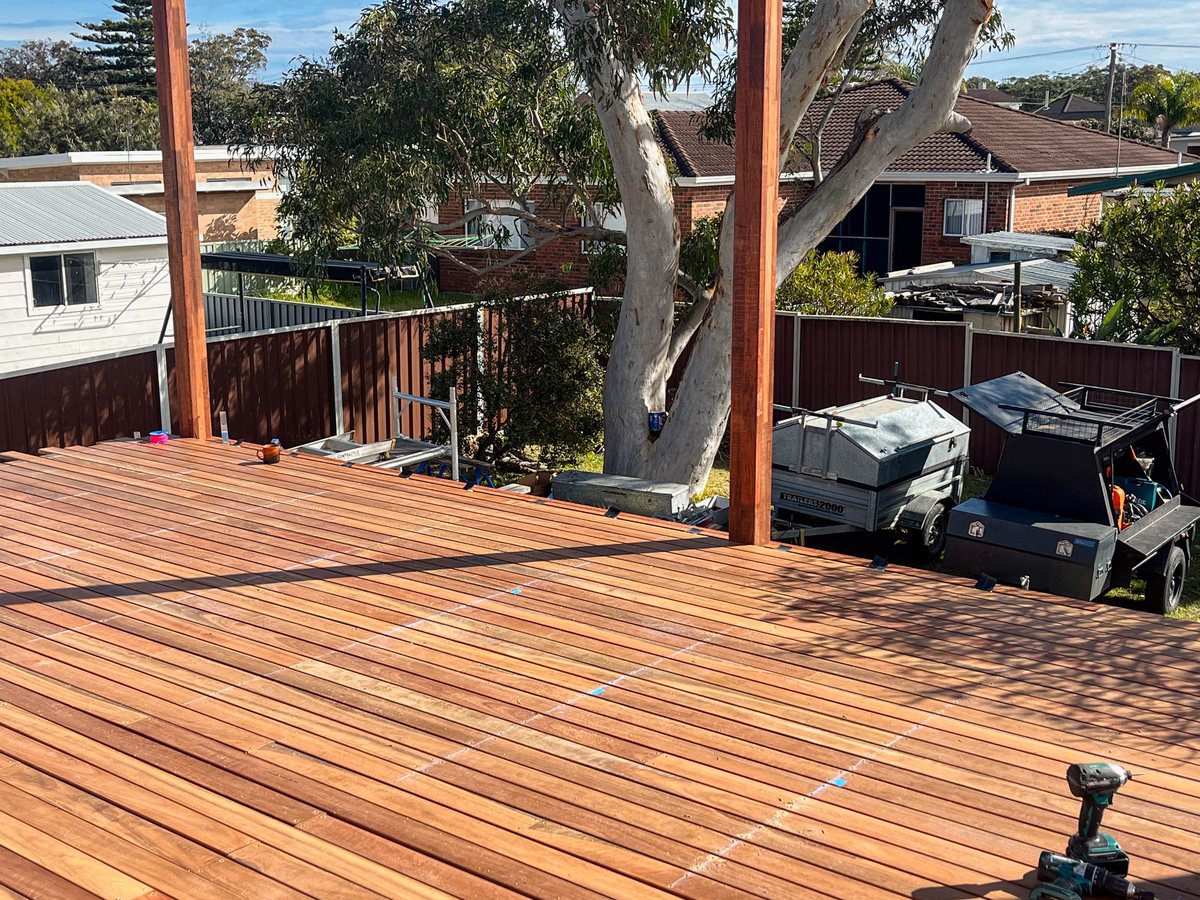 Timber decking laid between tall posts, with a drill and blue tape still on the surface.