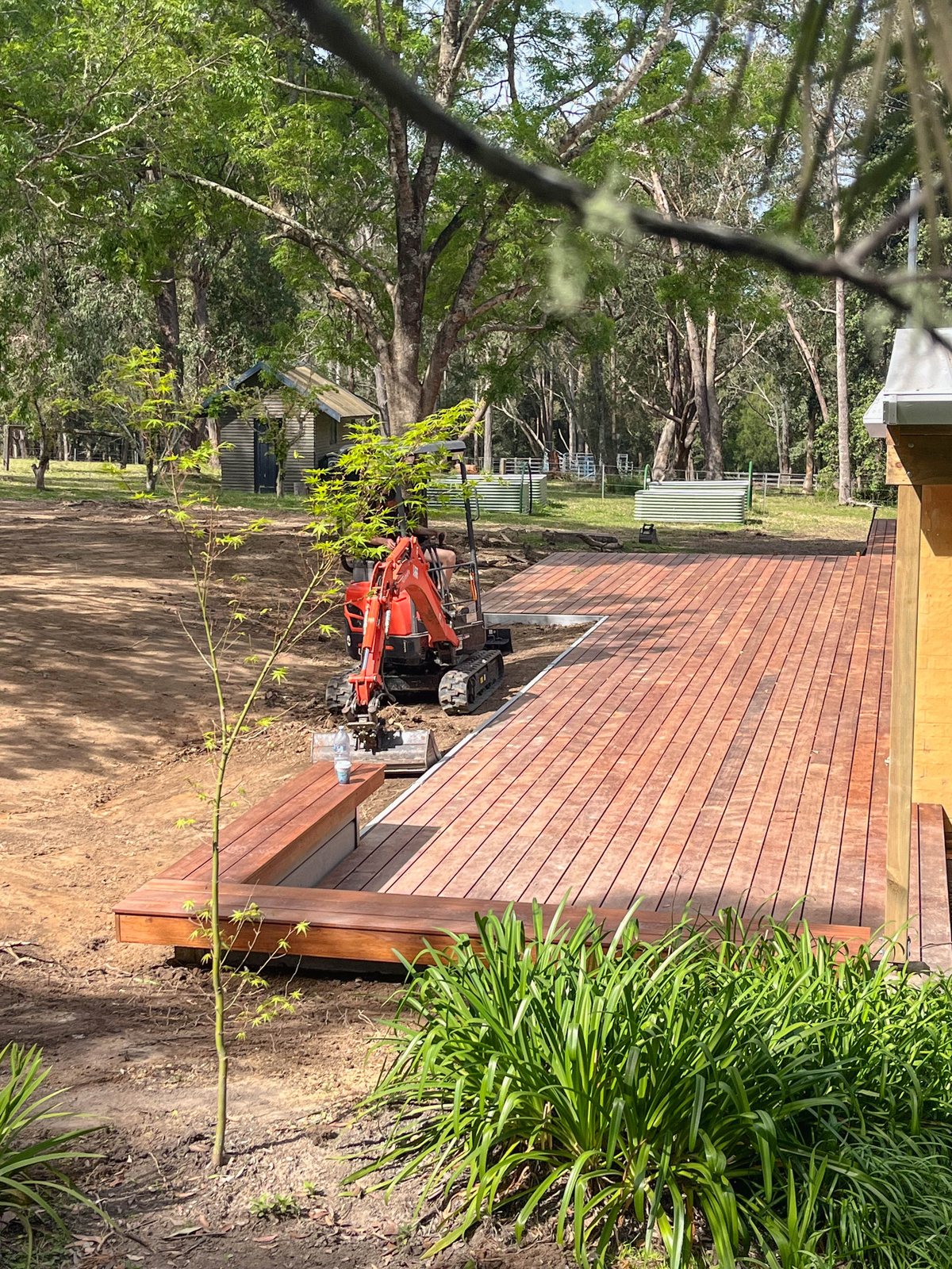 A timber deck beside exposed ground and a small excavator, with a low wall along one edge.