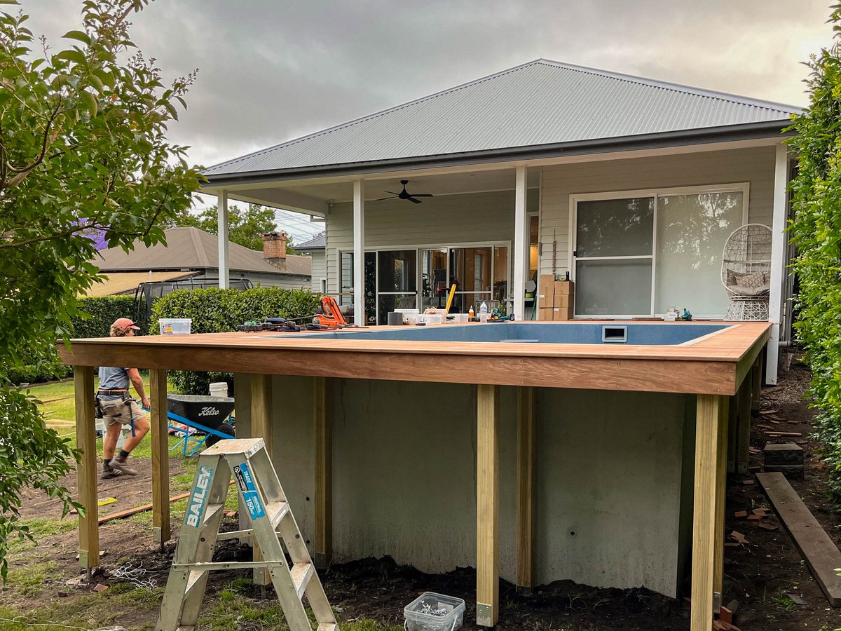 Timber decking around a raised pool, with the house behind, during construction.