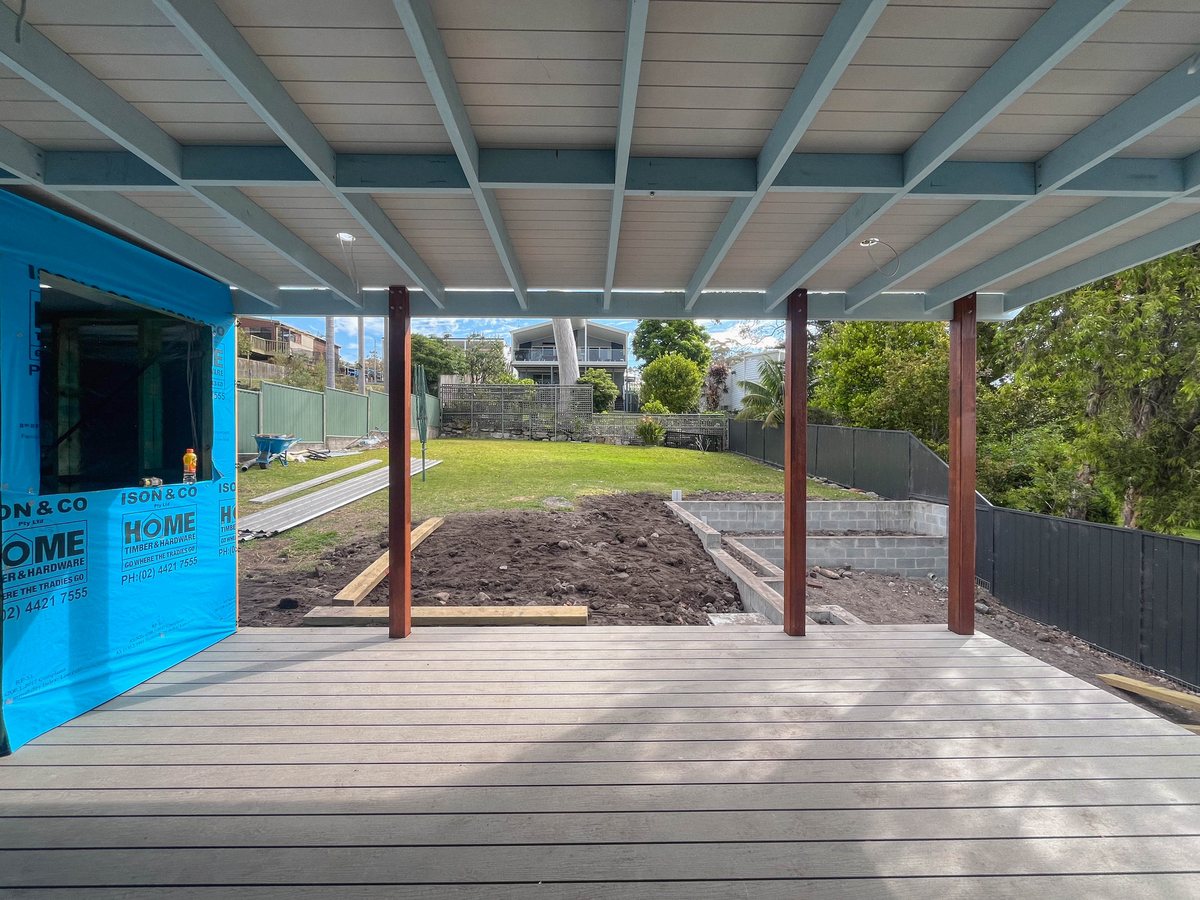 Grey decking beneath a ceiling with visible beams, with timber posts and building wrap beside the garden.