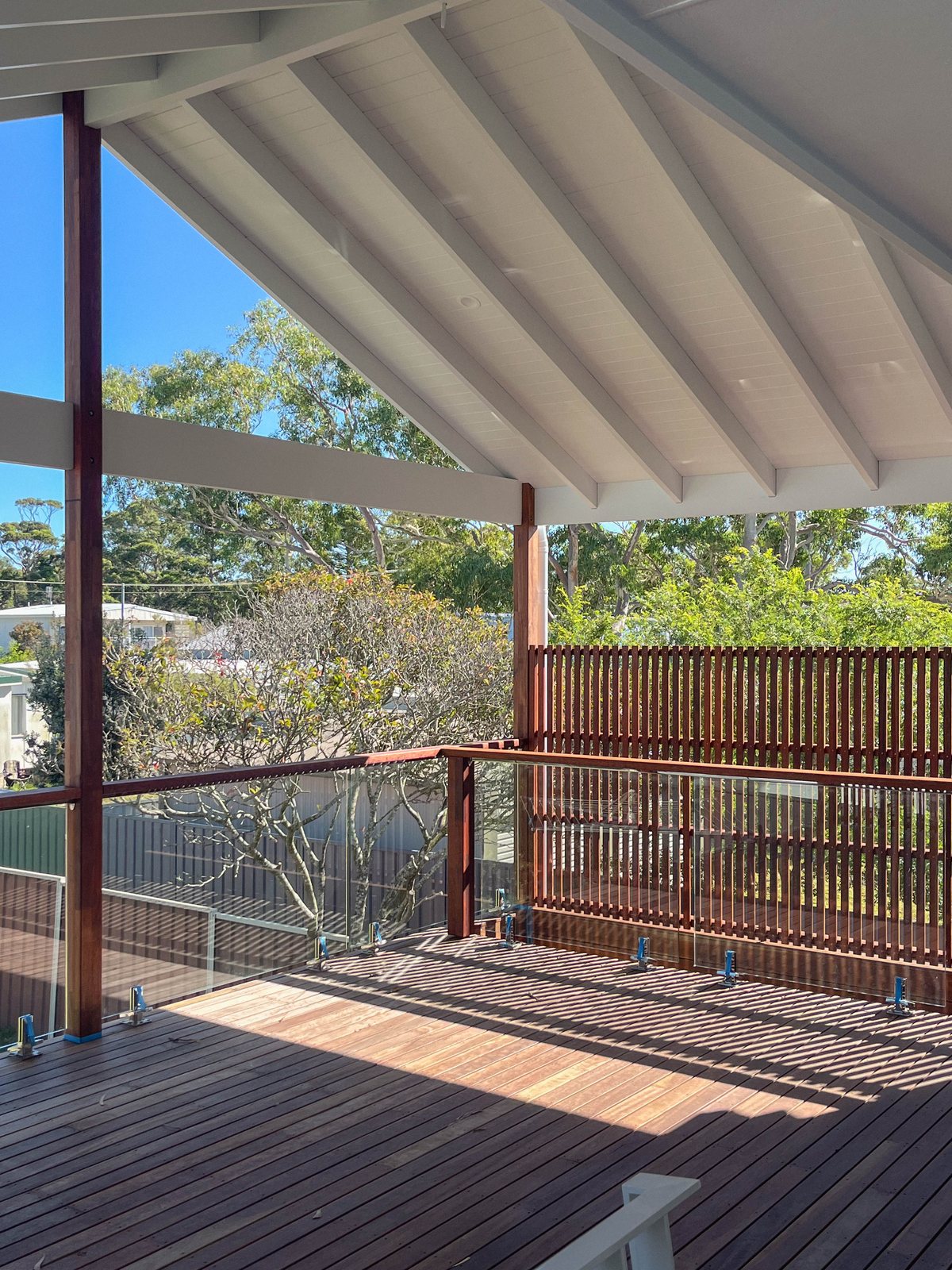 A deck beneath a white gable roof, with timber posts and a vertical slatted screen.