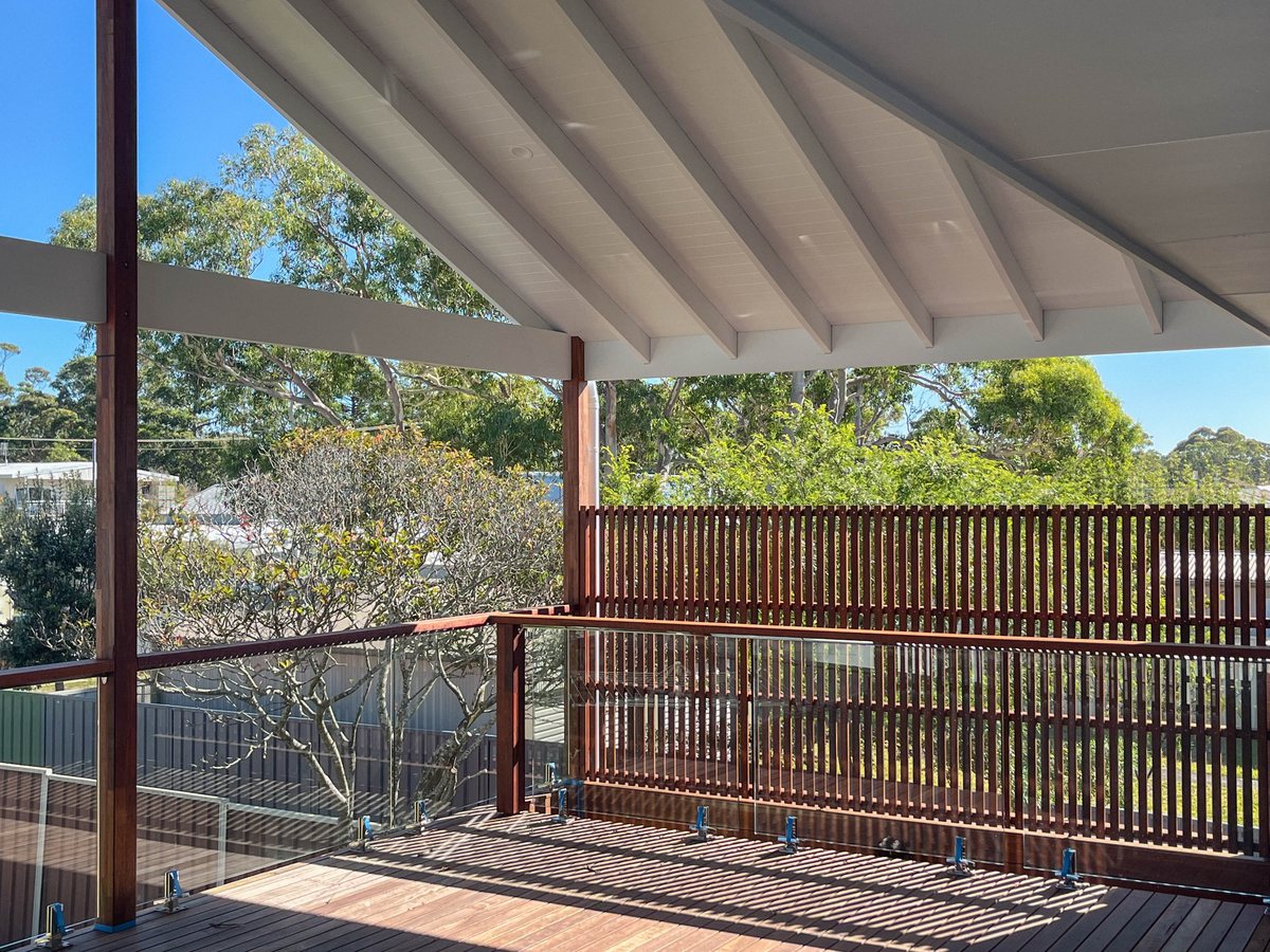 The underside of a white gable roof above timber posts and a vertical slatted screen.