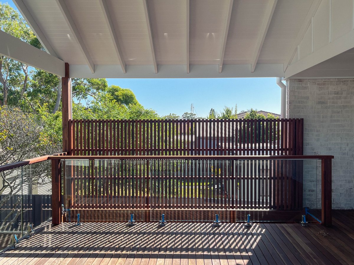 A vertical timber screen beneath a white roof, casting narrow shadows across the deck.