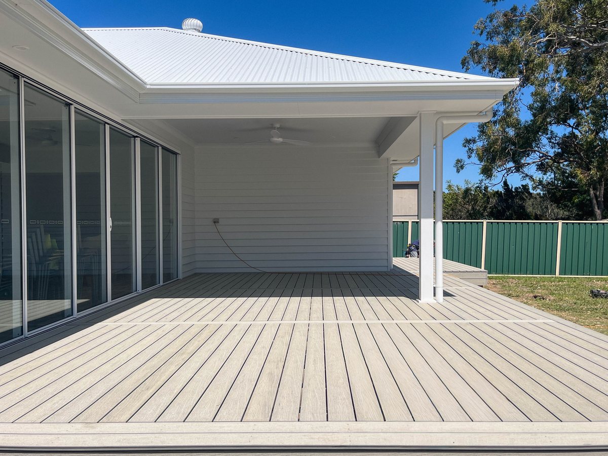 Grey decking beneath a white roof with square posts and a ceiling fan.