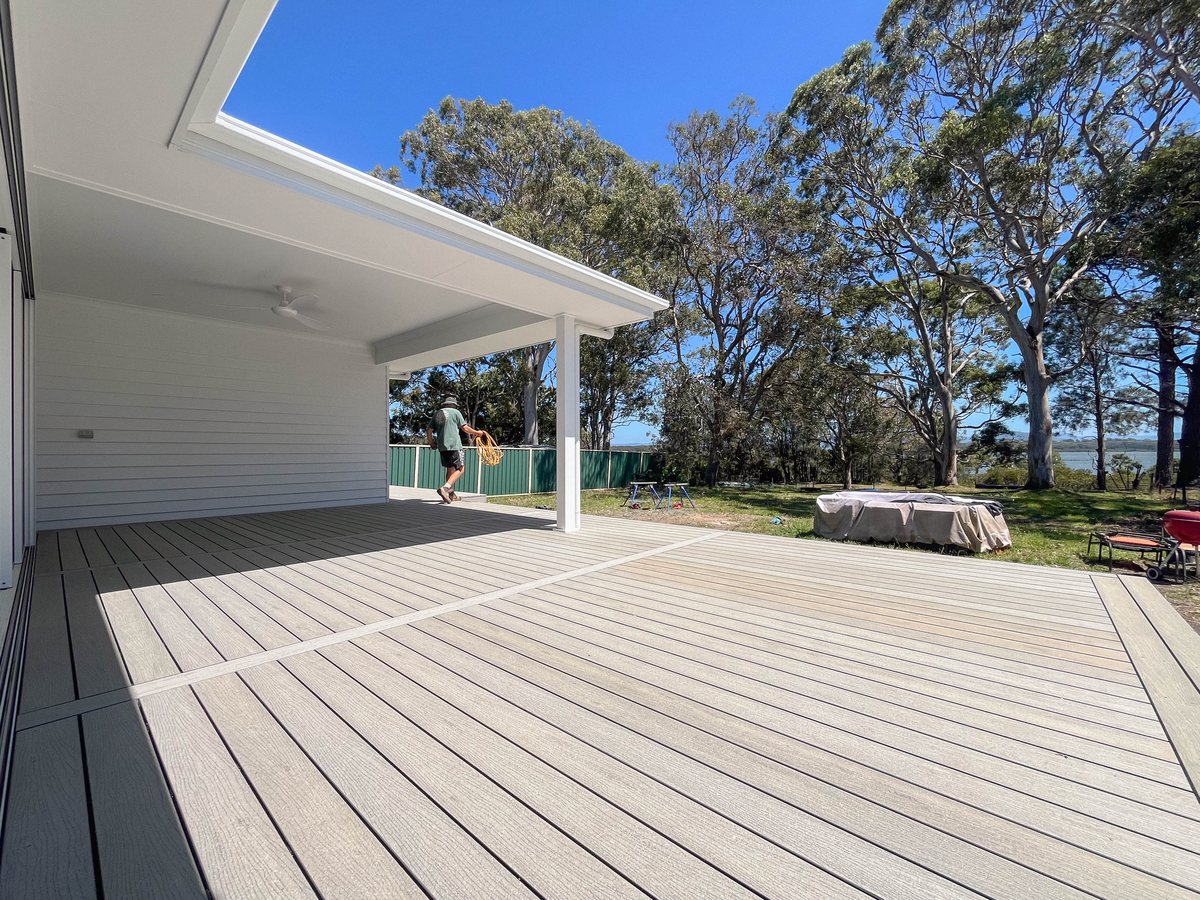 Grey decking extends from a white covered area towards a lawn and trees.